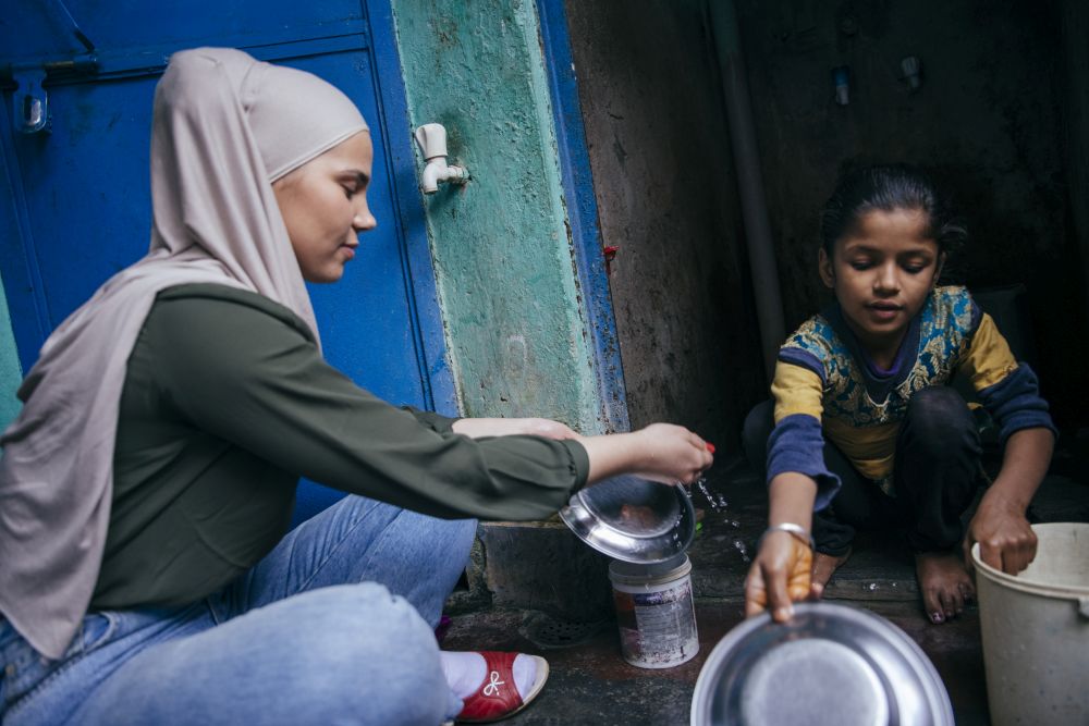 Iman meskini og enliten jente sitter på gulvet og vasker opp