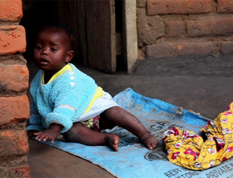 Liten-baby-leker-paa-bakken-utenfor-teglsteinhuset-i-Malawi