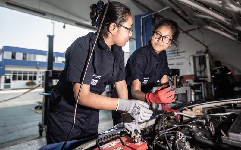 To unge jenter smiler til hverandre mens de jobber med en bilmotor