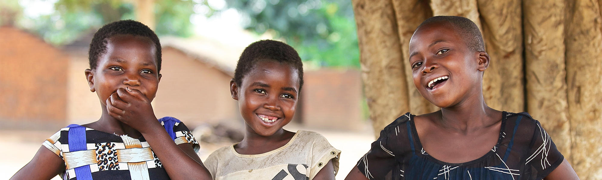 Tre jenter fra Malawi smiler og ler ute på en åpen plass