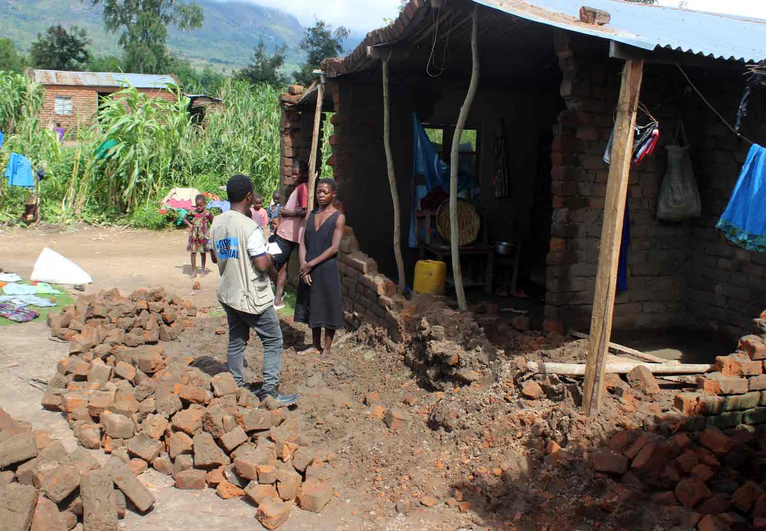 Bildet viser trebarnsmor Bertha fra Malawi utenfor familiens ødelagte hus, sammen med en arbeider fra Plan International