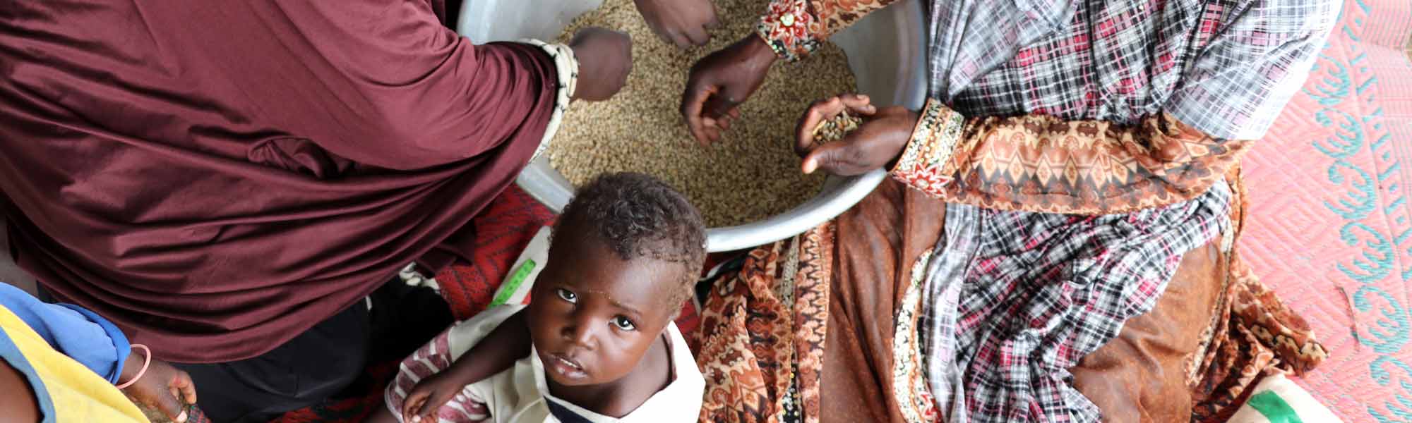 Kvinner i Niger som tilbereder mat og et lite barn, som ser opp mot kamera.