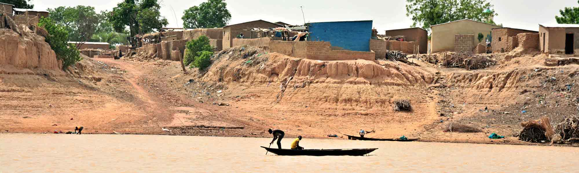 Landsby ved elven med to personer i en båt i Mali