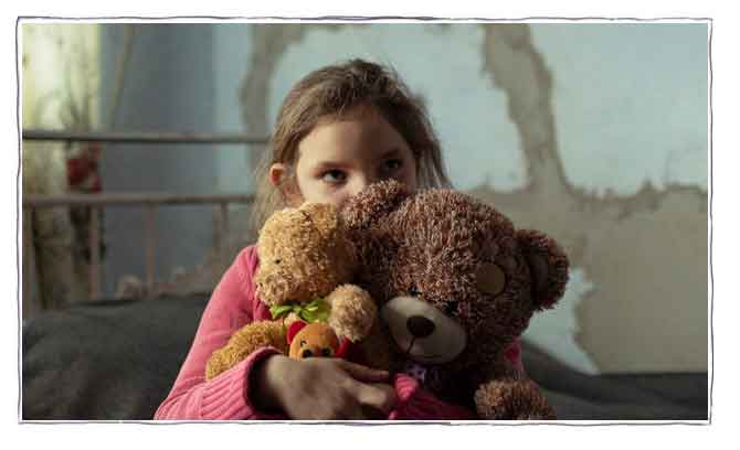 Jente fra Ukraina sitter i sengen sin med bamser