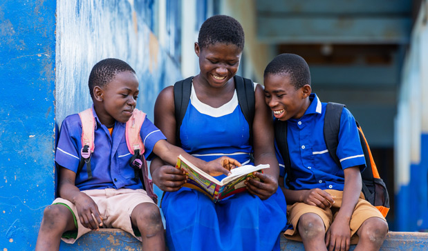 Jente leser med klassekompiser utenfor skolen i Ghana