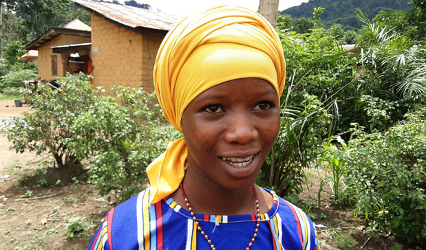 Jente smiler i hage fremfor hus i Guinea