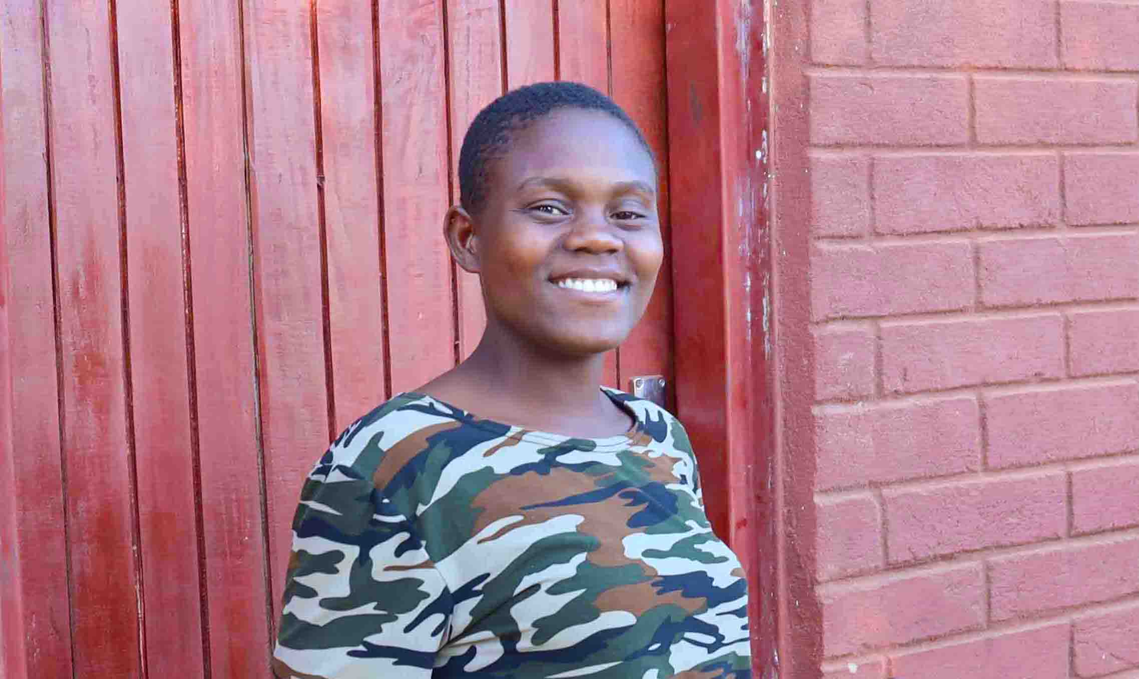 Jente smiler mot kamera utenfor bygg i Malawi