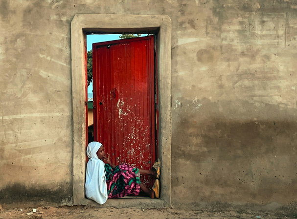 Jente sitter i døråpning utendørs i Nigeria
