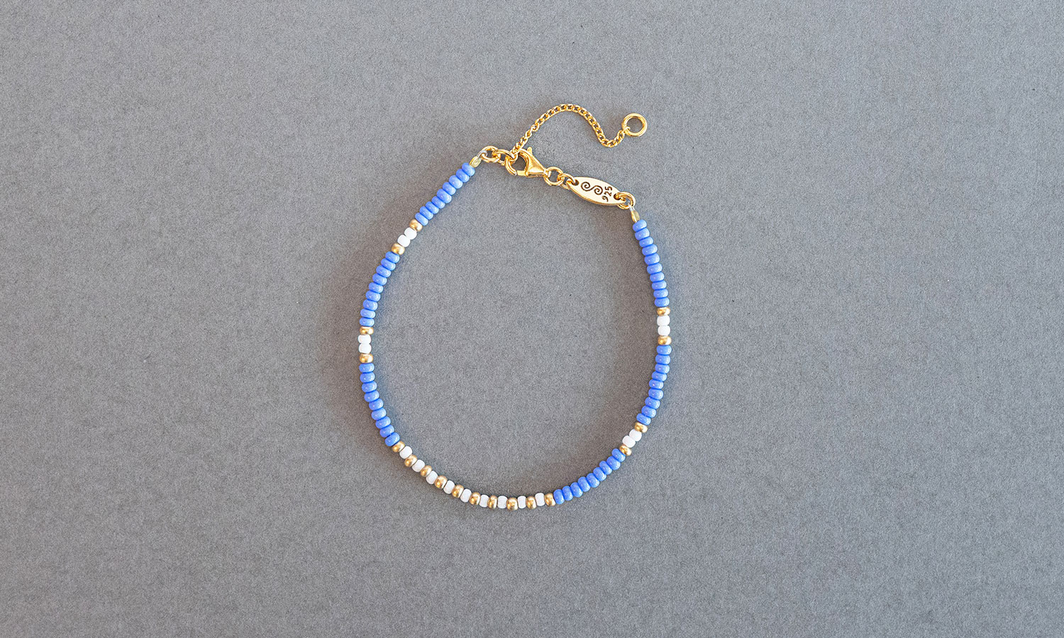 Gave med mening: Perlearmbånd med glassperler i blå, gull og hvit. Sølvlås. Foto.