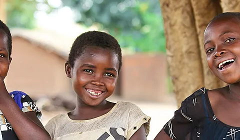 Tre jenter fra Malawi smiler og ler ute på en åpen plass