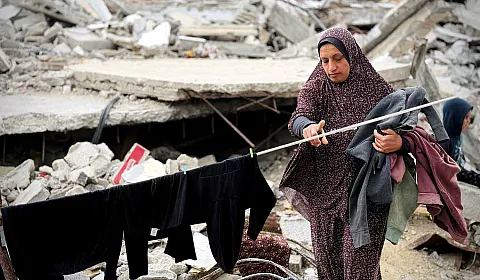 Kvinne henger opp klesvasken sin mellom ruiner av sammenraste bygninger i Gaza