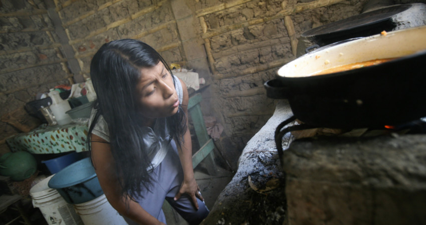 En jente blåser på flammene inne i ovnen for å få varme til å koke mat