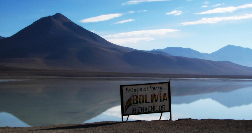 Skilt påskrevet Velkommen til Bolivia ved en innsjø og fjell i bakgrunnen