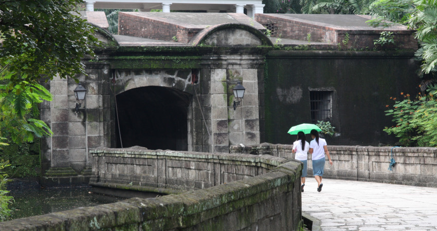 To jenter går under en grønn paraply på en gammel mur i Manila