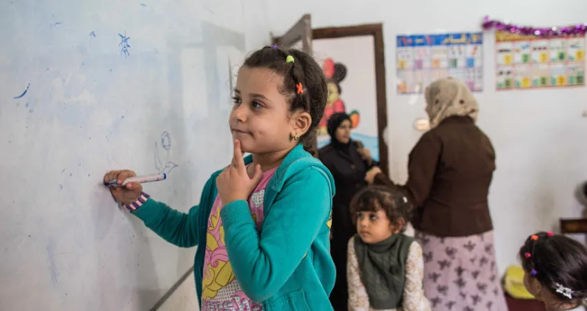 Girl standing in front of white borad with a pen in her hand at school