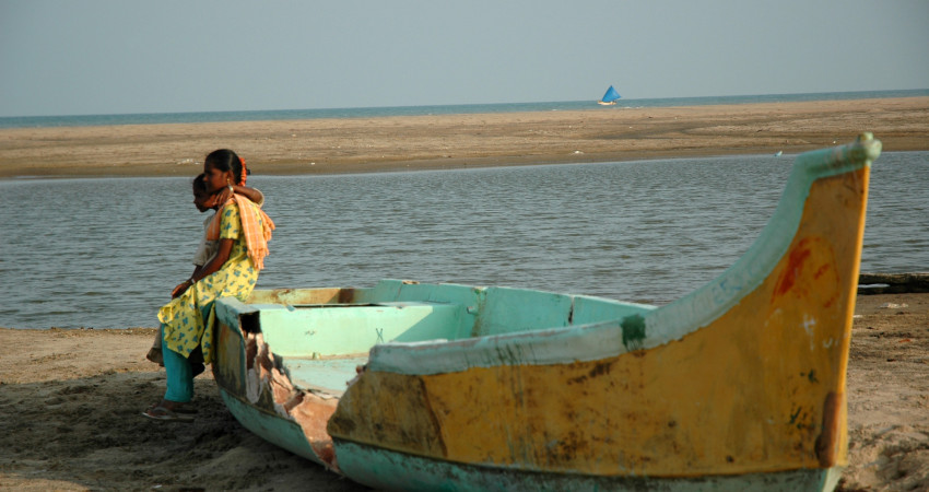 To jenter sitter på en båt som ligger på land, og ser utover havet