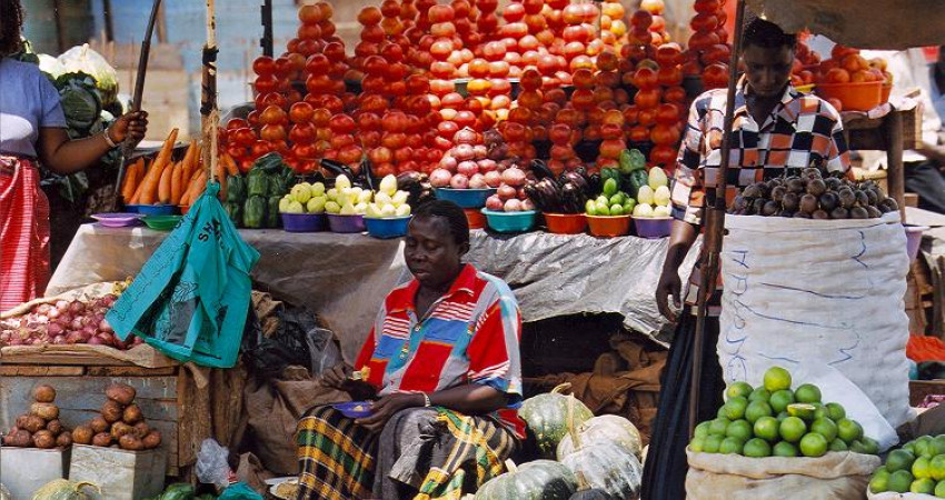 En mann sitter forann et tårn av tomater på markedet