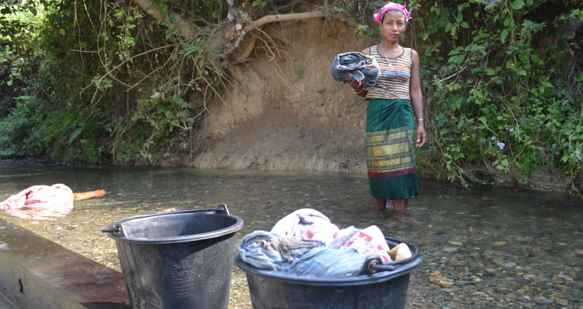 En kvinne står i elven med bøtter med klesvask