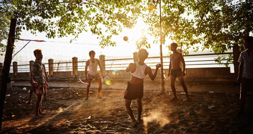 Gutter spiller fotball på standen i solnedgang
