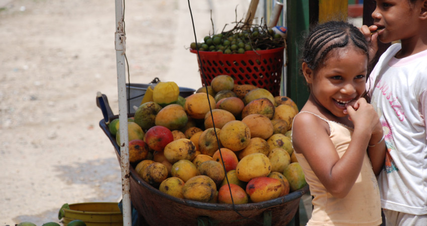 To jenter står ved siden av en trillebår fylt med mango