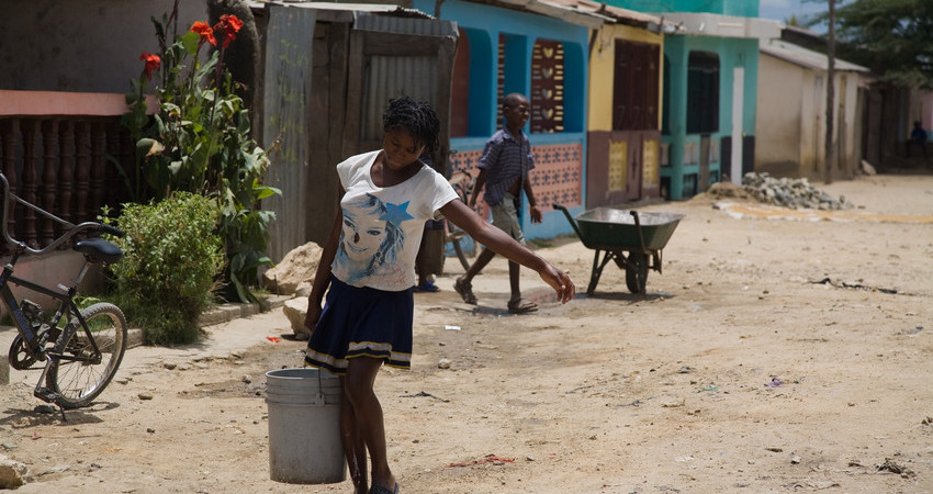 En jente går bortover en vei med en bøtte med vann