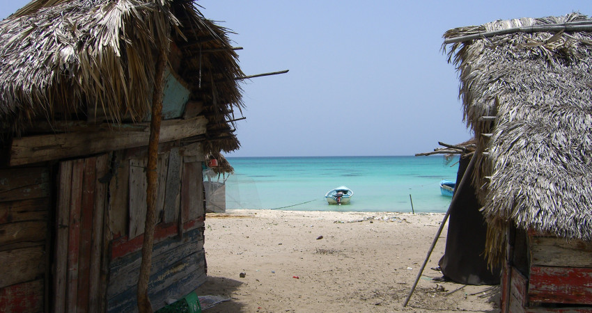 To små hus med palmetak på en strand rett ved havet