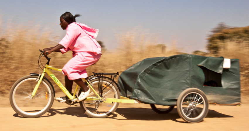Kvinne sykler på Zambulance - en sykkel med tilhenger som fungerer som transport for gravide og syke som må på sykehus.