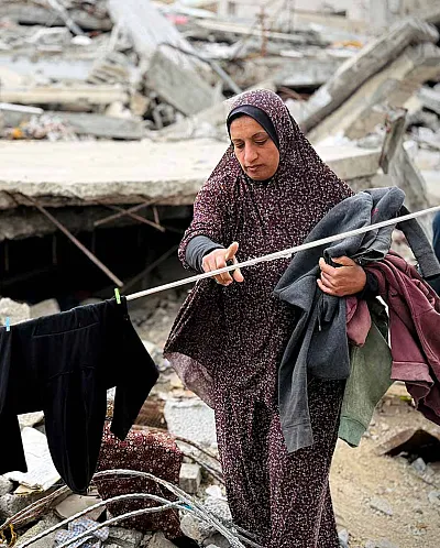 Kvinne tørker klær på klesnor omgitt av ruiner i Gaza