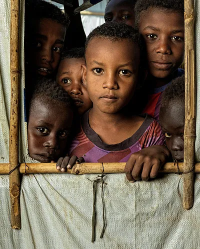Barn står inne i et telt og ser ut, i Sudan.