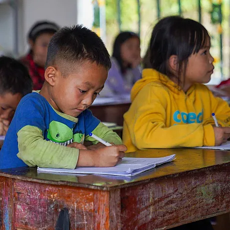 Ung elev skriver konsentrert notater i et klasserom