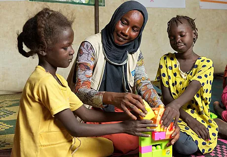 Plan-ansatt leker med to jenter i lekerom i flyktningeleir i Sør-Sudan