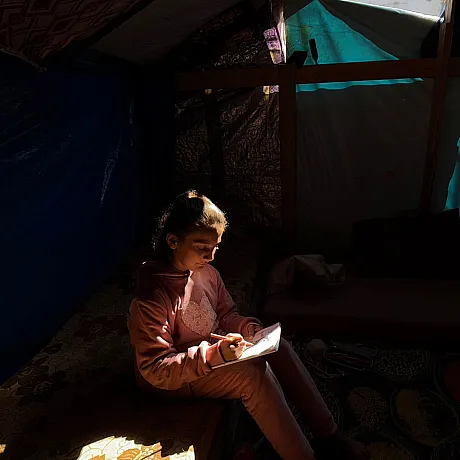 Jente sitter i et telt i Gaza og tegner