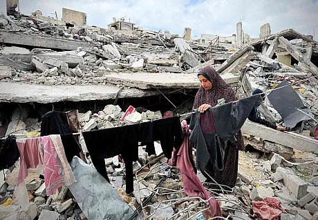 Kvinne henger opp klesvasken sin mellom ruiner av sammenraste bygninger i Gaza