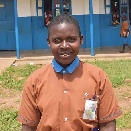 Jente fra Uganda står foran skolen sin