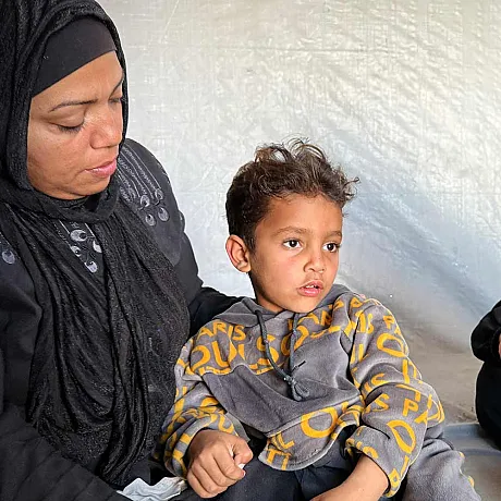 Mor, lillebrod og søster sitter inne i et telt i Gaza