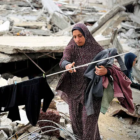 Kvinne tørker klær på klesnor omgitt av ruiner i Gaza
