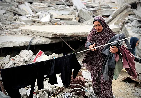 Kvinne tørker klær på klesnor omgitt av ruiner i Gaza
