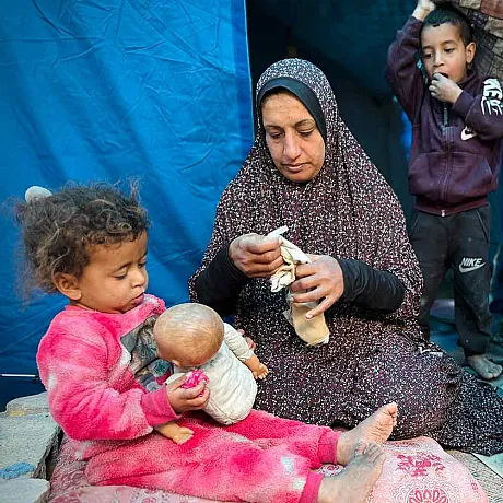 Mor sitter med tre barn utenfor et telt i Gaza
