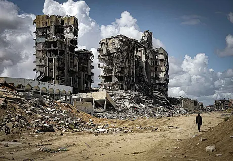 Bombede bygg i Gaza og person som går langs veien