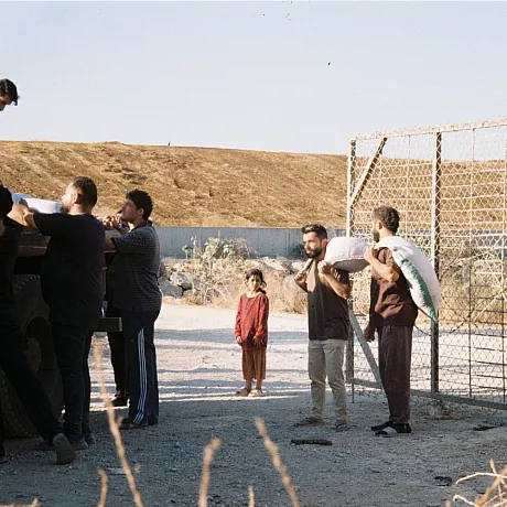 Ei jente står i bakgrunnen og ser på at menn henter matforsyninger.