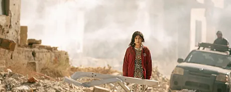 Jente står blant ruiner og bombede hus i Libanon.