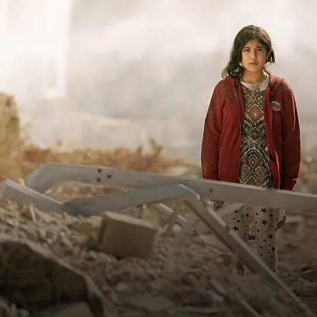 Jente står blant ruiner og bombede hus i Libanon.