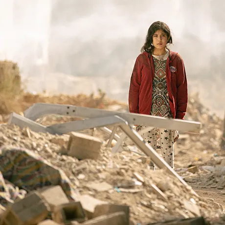 Jente står blant ruiner og bombede hus i Libanon.