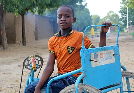 Gutt fra Kamerun som sitter på rullestolstykkel.