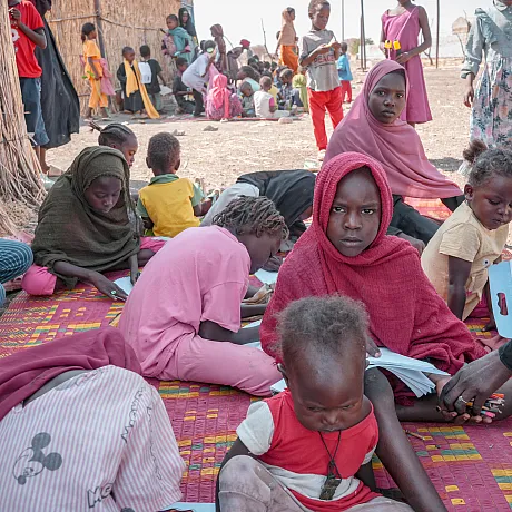Barn sitter på bakken i en flyktningleir i Sudan