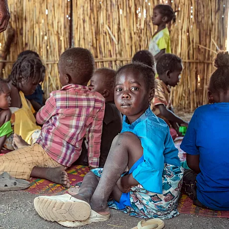 Jente fra Sudan sitter på bakken og ser i kamera