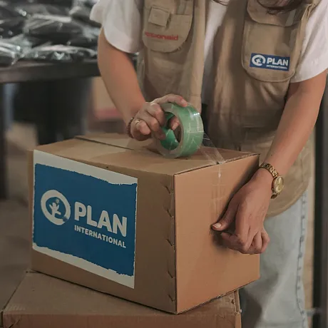 Person som teiper igjen en eske med Plan-logo.