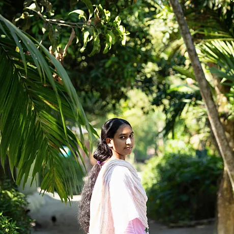 Jente i Bangladesh står utendørs med grønne planter rundt seg.