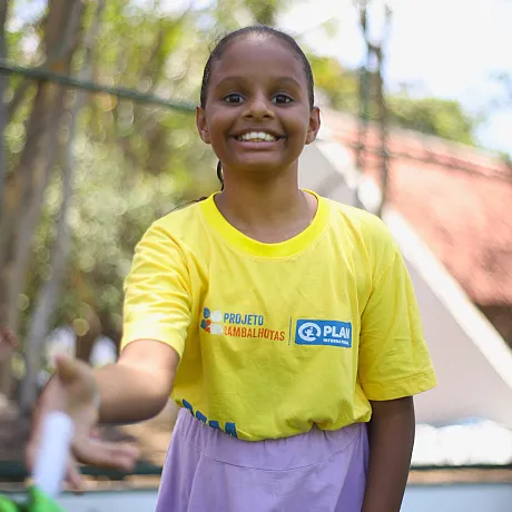 Jente Brasil med gul t-skjorte leker utendørs.