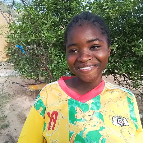 Jente i gul og grønn genser står fremfor busk i Burkina Faso.